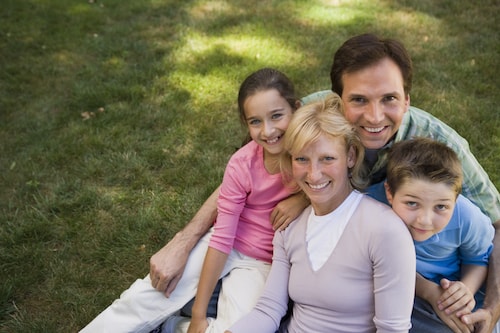 A family huddled lovingly in the grass and smiling because of the exceptional family dentistry they receive in Anchorage from Fireweed Family Dentistry